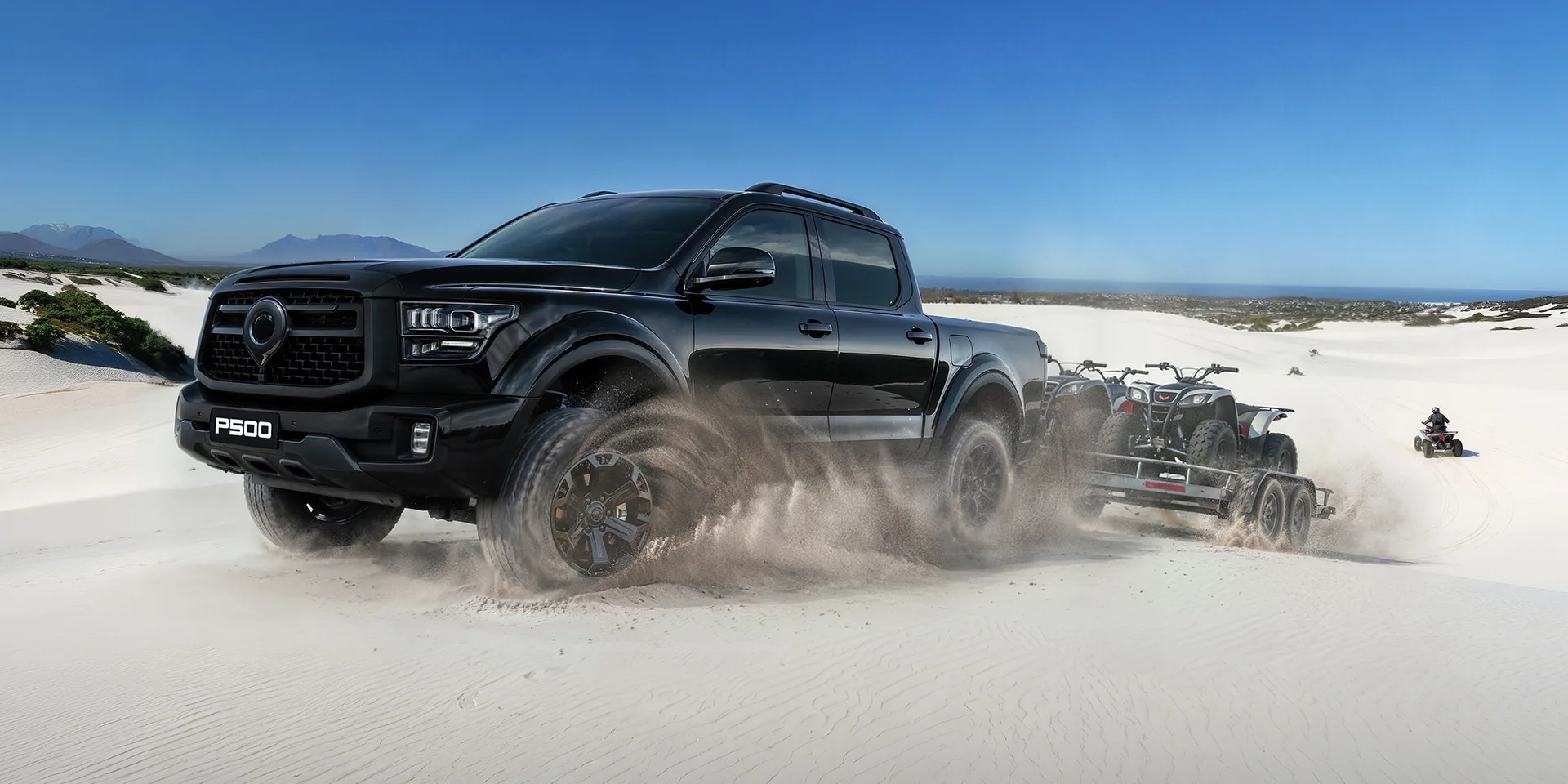 GWM P500 towing quad bikes through sunlit white dunes beside the coast
